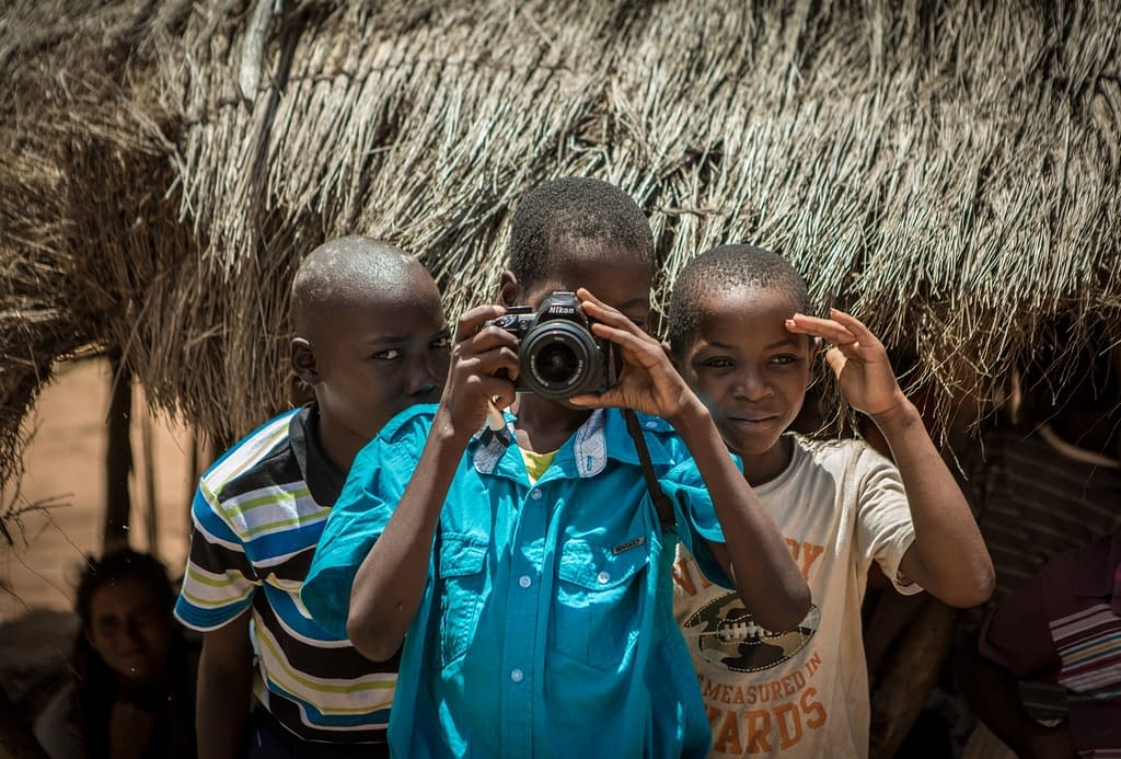 Child takes a photo of the photographer with two other children watching next to him