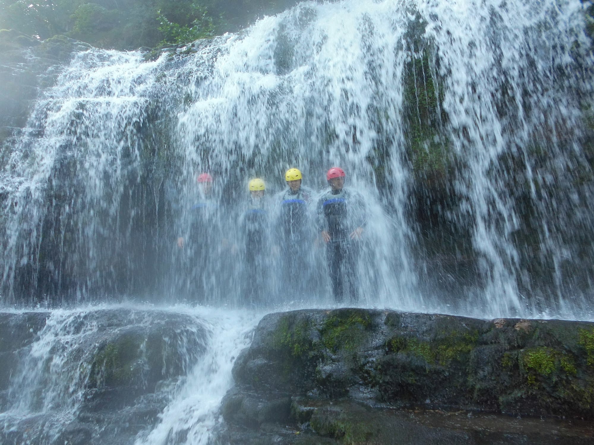 Group standing under large waterfall whilst canyoning